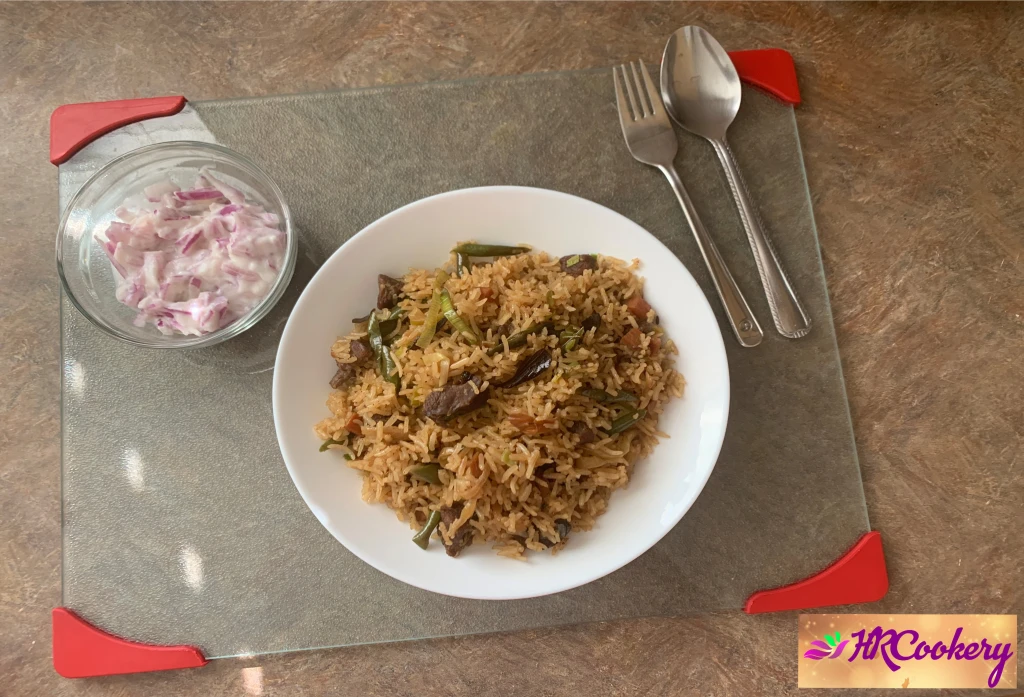 Plate of beef fried rice with tender beef strips, peas, carrots, scallions, and sesame seeds, showcasing a glossy, savory stir-fry.