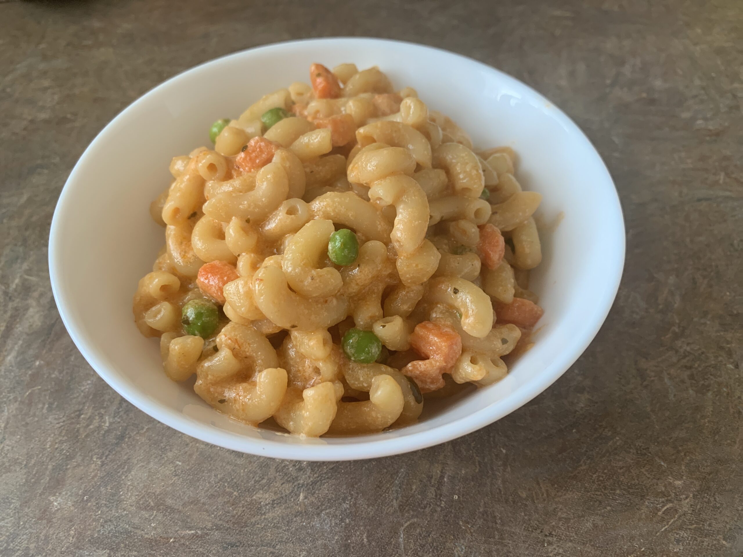 Bowl of creamy mac and cheese topped with a sprinkle of parsley and melted cheese, served with a fork on the side.
