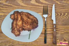 A bowl of mayo marinated chicken pieces coated in a creamy mixture, garnished with fresh herbs, with whole spices scattered around on a wooden surface.