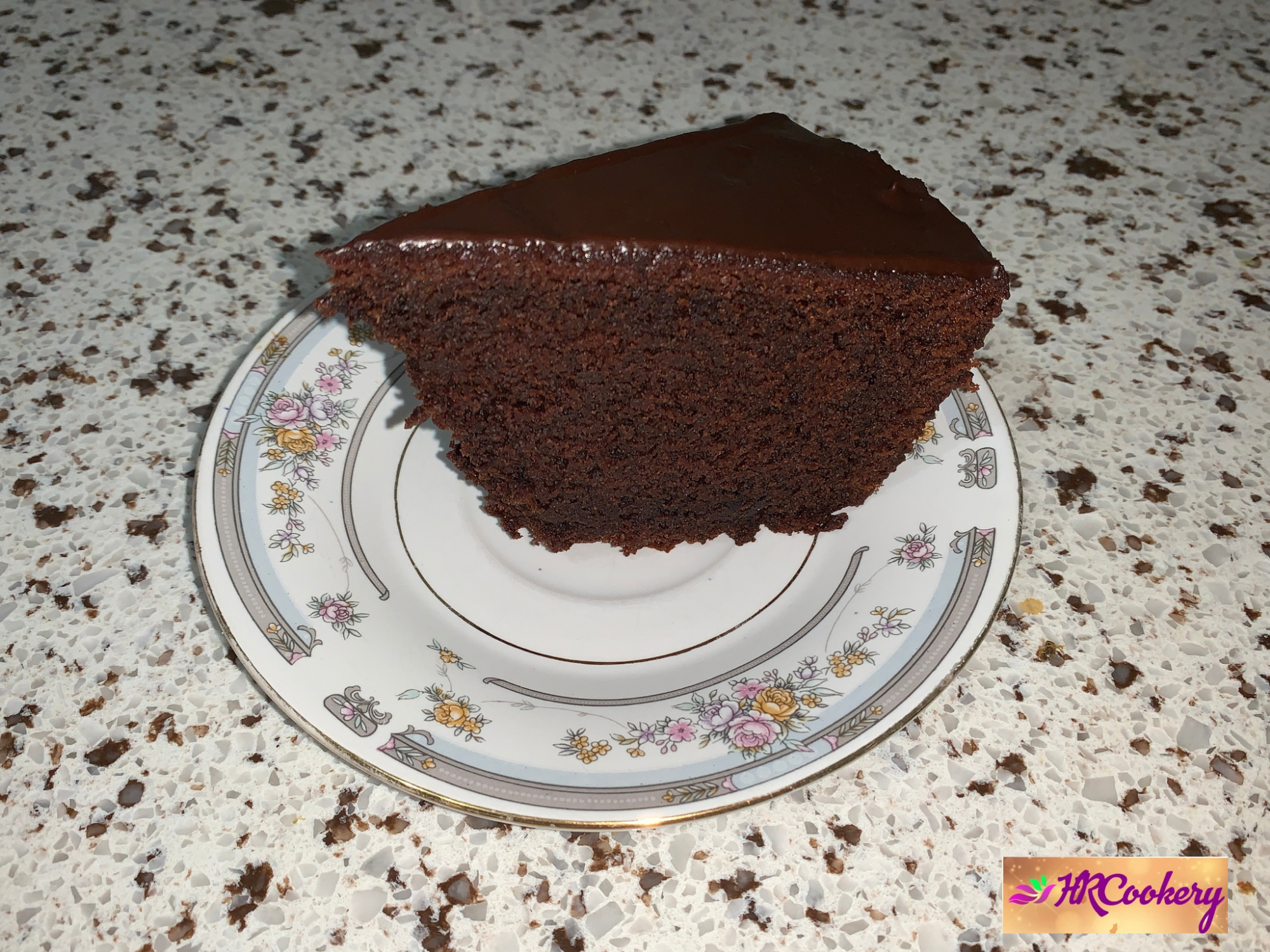 A rich chocolate mud cake slice on a white plate, garnished with a dollop of whipped cream and a sprinkle of cocoa powder, with a fork beside it.