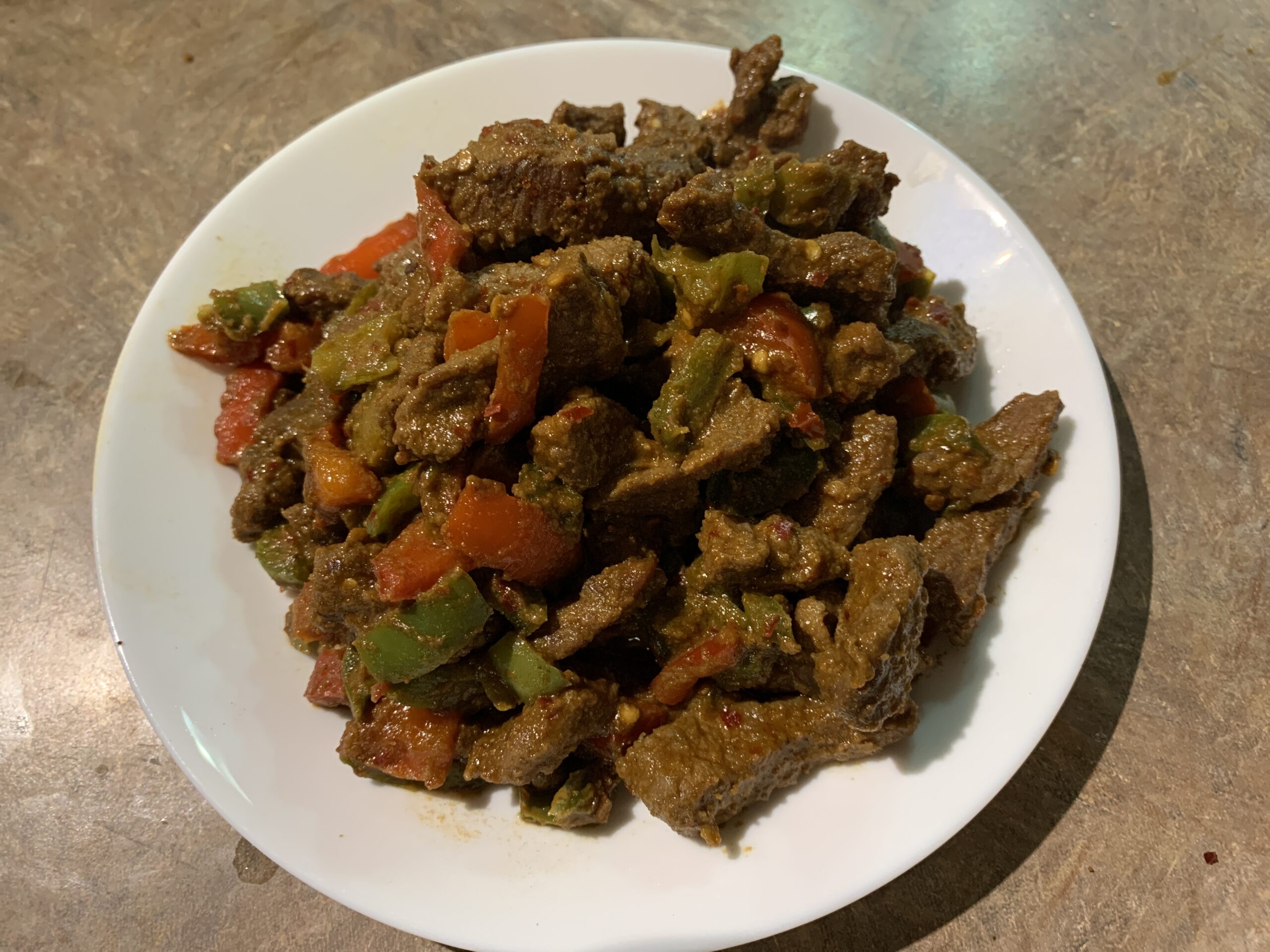 Plate of cumin-spiced beef strips garnished with fresh cilantro, accompanied by colorful bell peppers and onions, served with a side of rice.