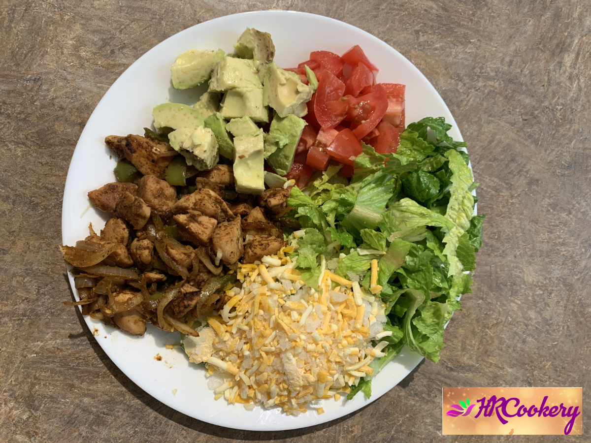 A colorful keto chicken fajita salad in a bowl, featuring grilled chicken slices, bell peppers, avocado, lettuce, and a sprinkle of lime juice.