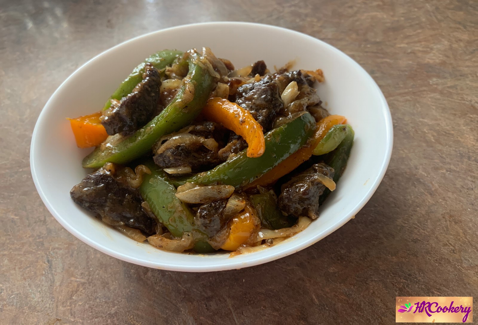 A white bowl filled with black pepper beef stir-fry, featuring tender beef slices, bell peppers, and a glossy black pepper sauce.
