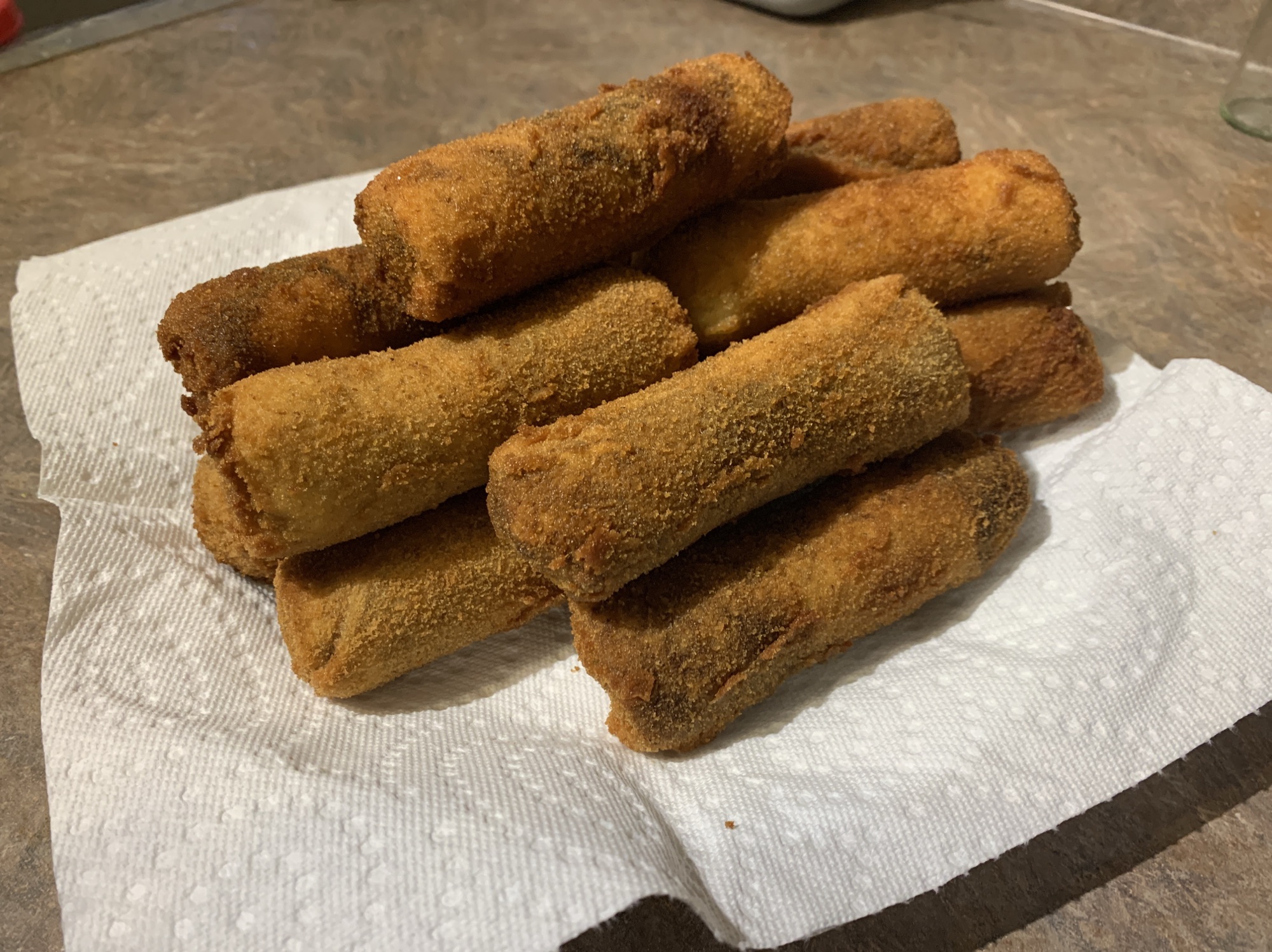 A plate of freshly made Sri Lankan beef rolls, showcasing their crispy golden-brown exterior, served with a side of dipping sauce and garnished with fresh herbs.