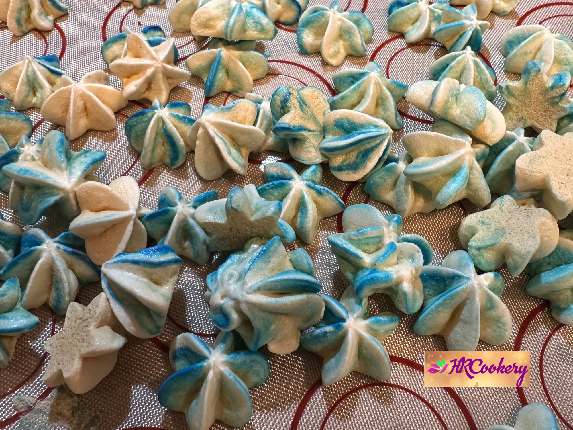 Freshly baked blue and white meringue cookies on a baking mat.
