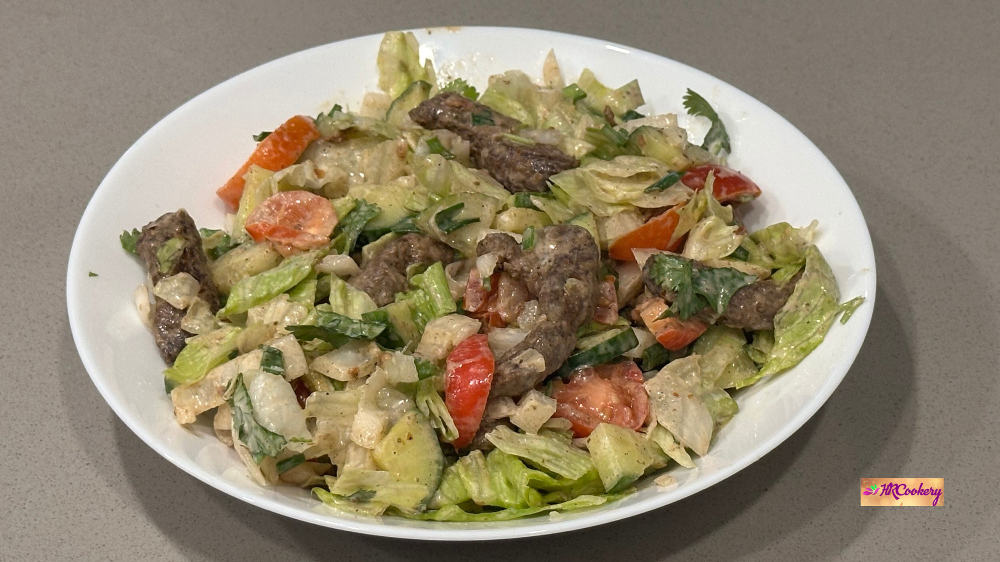 Creamy beef salad with lettuce, tomatoes, cucumber, and herbs in a white bowl
