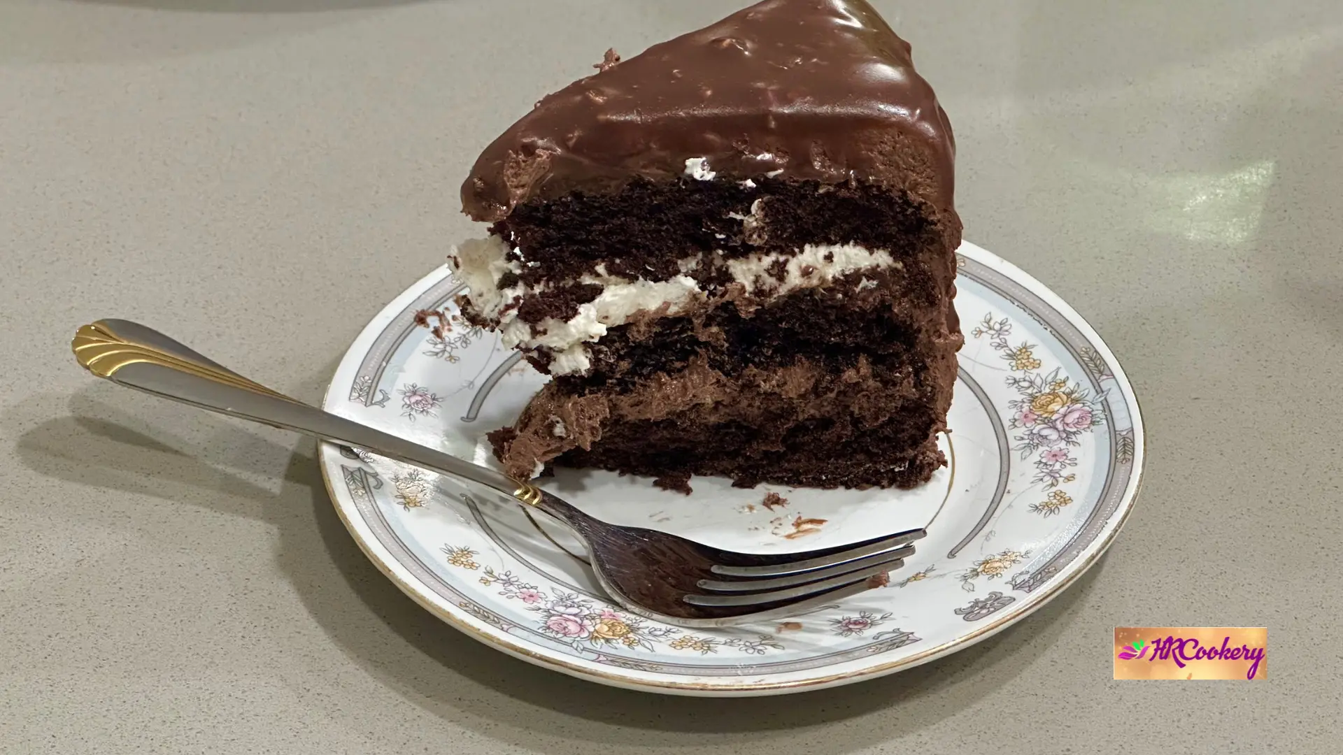 Slice of ultimate fudge chocolate layer cake with creamy frosting and ganache on a plate