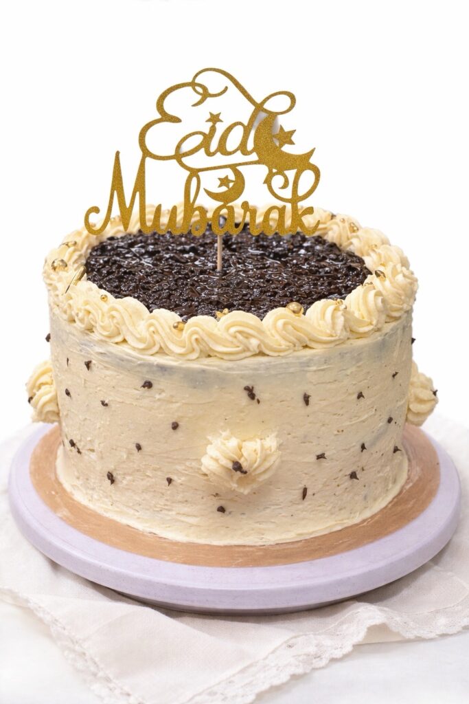 Black velvet cake with vanilla Swiss meringue buttercream frosting decorated with chocolate chips and a gold Eid Mubarak topper