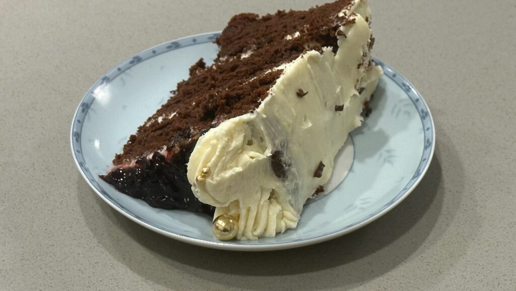 Slice of black velvet cake with vanilla Swiss meringue buttercream and berry filling on a plate